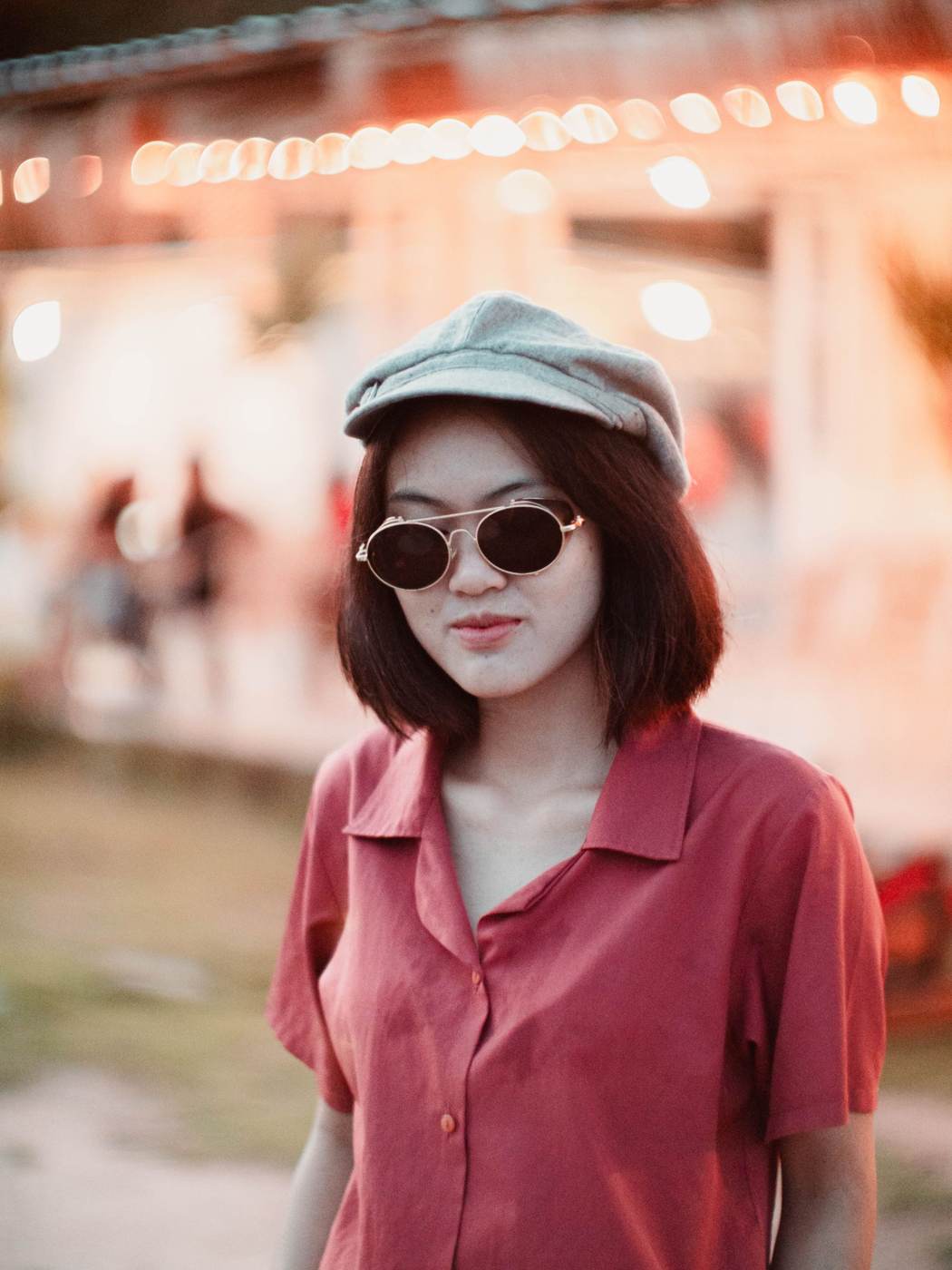 Demonstration photograph. A woman in a cap and round sunglasses, city lights out of focus behind her.