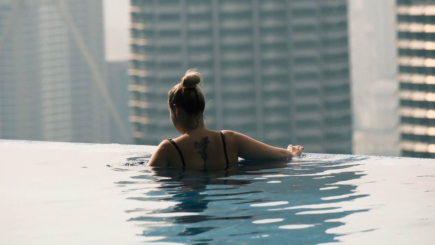 Demonstration photograph. A woman in a rooftop pool with tower blocks rising behind her.