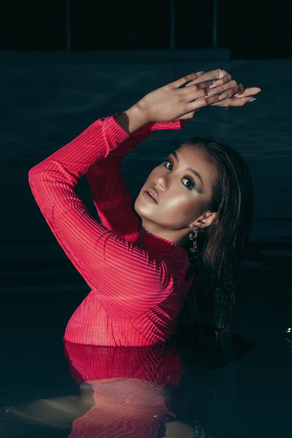 Demonstration photograph. A model in a red mesh top photographed in dark water, arms raised.