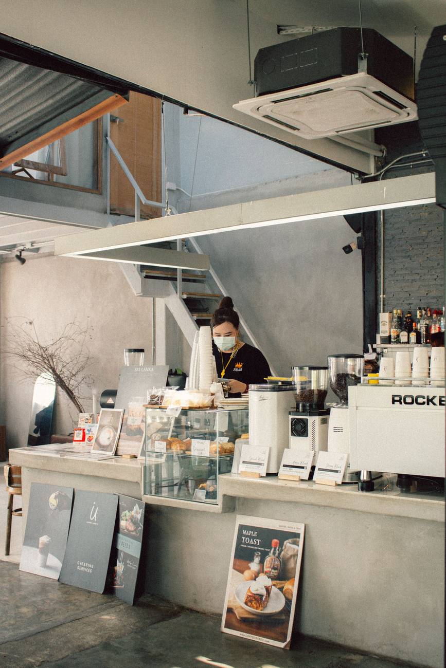 Demonstration photograph. A person working behind a cafe counter seen from the street, espresso machines in front of them.