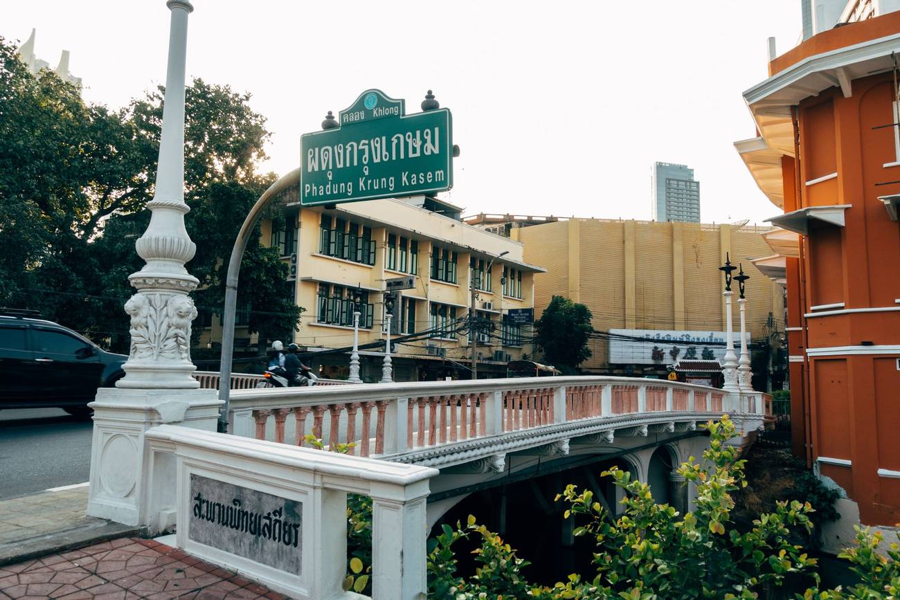 Demonstration photograph. A stone bridge over a canal with Thai signage and city buildings behind.