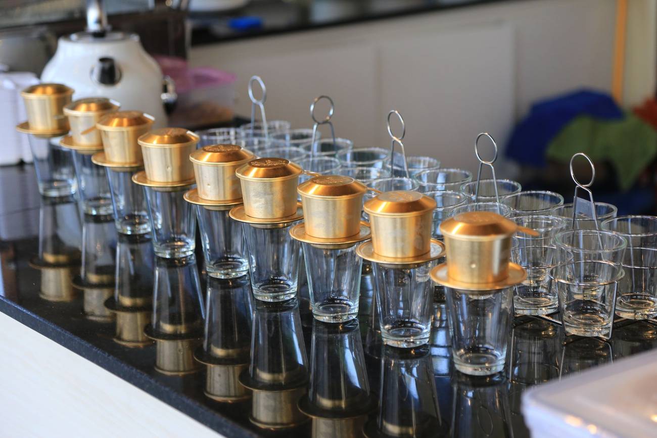 Demonstration photograph. Rows of glasses with metal coffee filters set out along a counter.