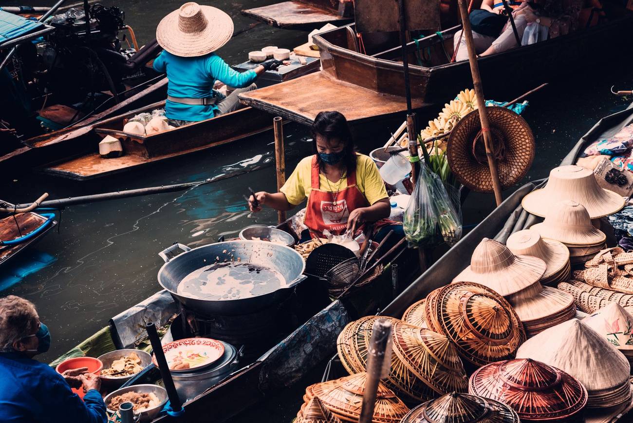 Demonstration photograph. A woman cooking on a boat at a floating market, surrounded by pans and baskets.