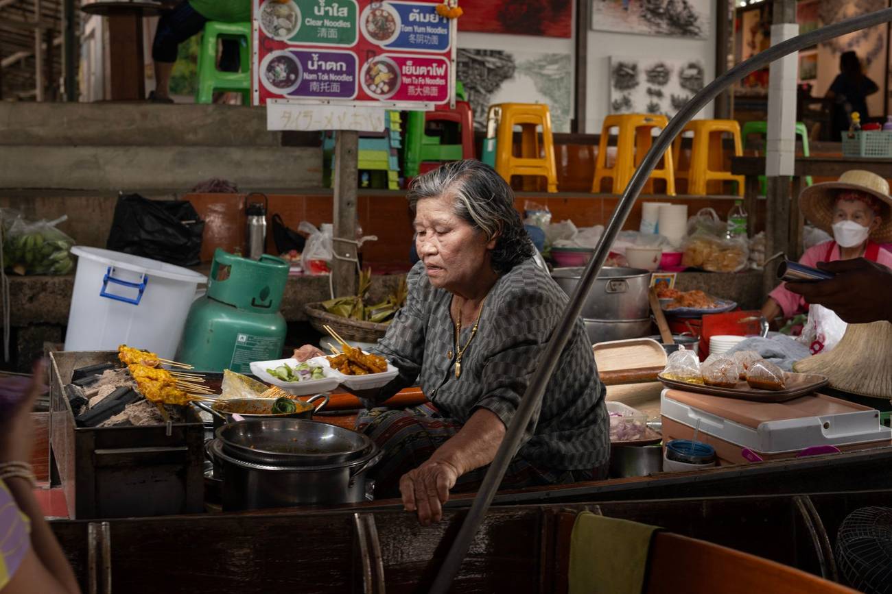 Demonstration photograph. An older woman working at a street food stall, cooking over a pan.