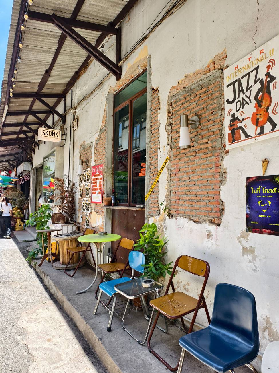 Demonstration photograph. A narrow lane with mismatched chairs and small tables set out against a painted wall.